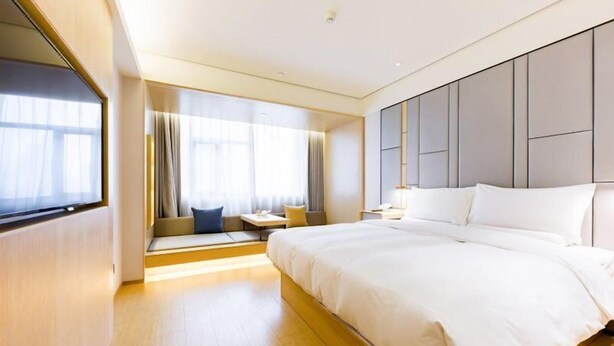 Una habitación de hotel moderna con una cama grande, una zona de estar con vistas y un ventanal amplio.