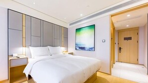 Una habitación de hotel moderna con una cama grande, una mesita de noche, un cuadro en la pared y una puerta de madera.