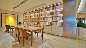 A modern interior with a wooden dining table, chairs, a laptop, and a bookshelf with illuminated shelves. - Ji Hotel (Jinan)