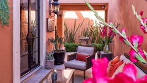 A cozy outdoor seating area with a glass table, a cushioned chair, and a sofa. There are potted plants and a decorative lamp. - Luxury Villa B&B (San Miguel de Allende)