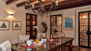 A dining room with a glass table, chairs, and a chandelier. There are framed artworks on the walls and a large window with a view. - Luxury Villa B&B (San Miguel de Allende)