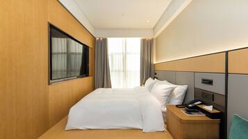Quarto de hotel com uma cama grande, mesa de cabeceira com telefone e controle remoto, janela com cortinas e vista para o exterior.