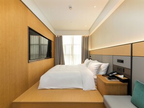 Quarto de hotel com uma cama grande, mesa de cabeceira com telefone e controle remoto, janela com cortinas e vista para o exterior.