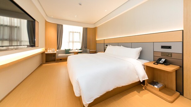 Een moderne hotelkamer met een groot bed, nachtkastje met telefoon en raam met gordijnen.