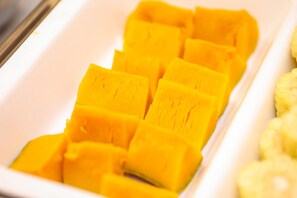 Uma tigela branca e retangular com várias fatias de fruta amarela, provavelmente manga, dispostas de forma organizada.