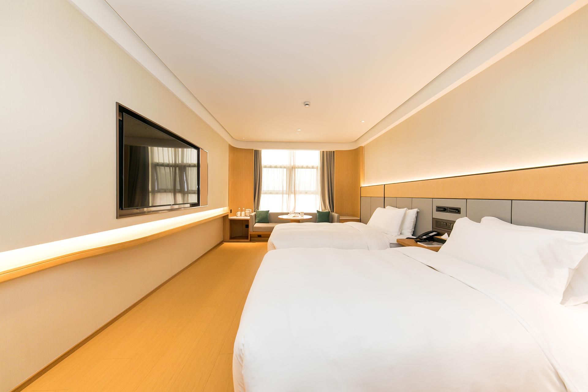 Habitación de hotel con dos camas, un televisor, una mesita de noche, una lámpara y un ventanal con cortinas.