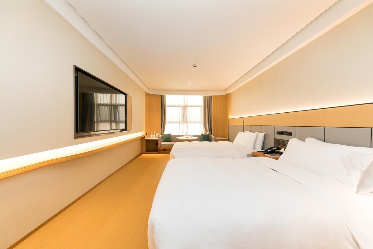Une chambre d’hôtel avec deux lits, une télévision, une table de chevet, une lampe et une fenêtre avec des rideaux.
