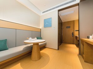 A modern hotel room with a seating area, a round table, and a door leading to a bathroom.