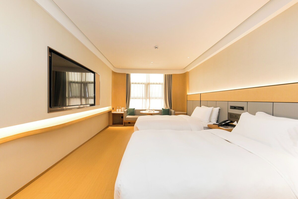 Une chambre d’hôtel avec deux lits, une télévision, une table de chevet, une fenêtre avec des rideaux et un petit coin salon.