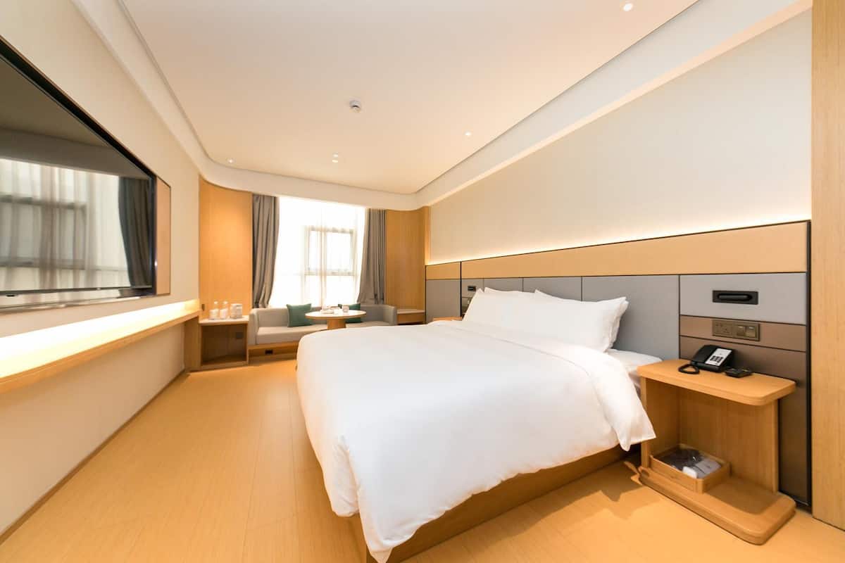 A modern hotel room with a large bed, bedside table with a phone, and a window with curtains.