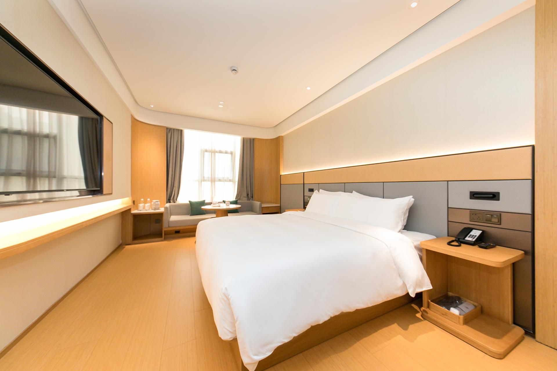 Una habitación de hotel moderna con una cama grande, una mesita de noche con teléfono y una ventana con cortinas.