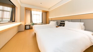 Een hotelkamer met twee bedden, een nachtkastje met een telefoon, een tafeltje met een lamp en een raam met gordijnen.