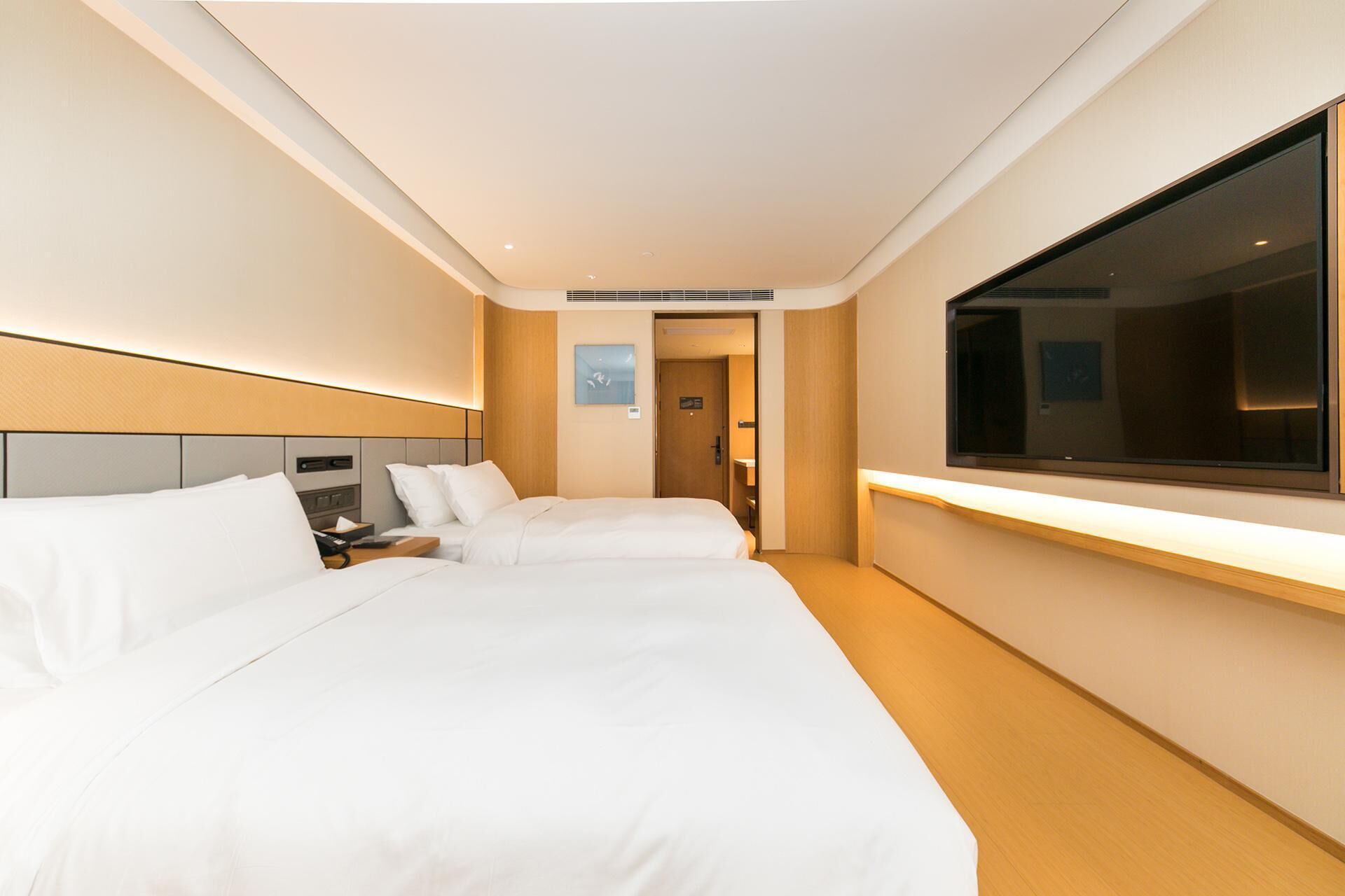Quarto de hotel com duas camas, uma janela grande e uma mesa de cabeceira.