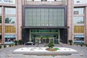 A hotel entrance with a modern facade, a car parked in front, and a landscaped area with rocks and a tree. - JI Hotel (Hangzhou)