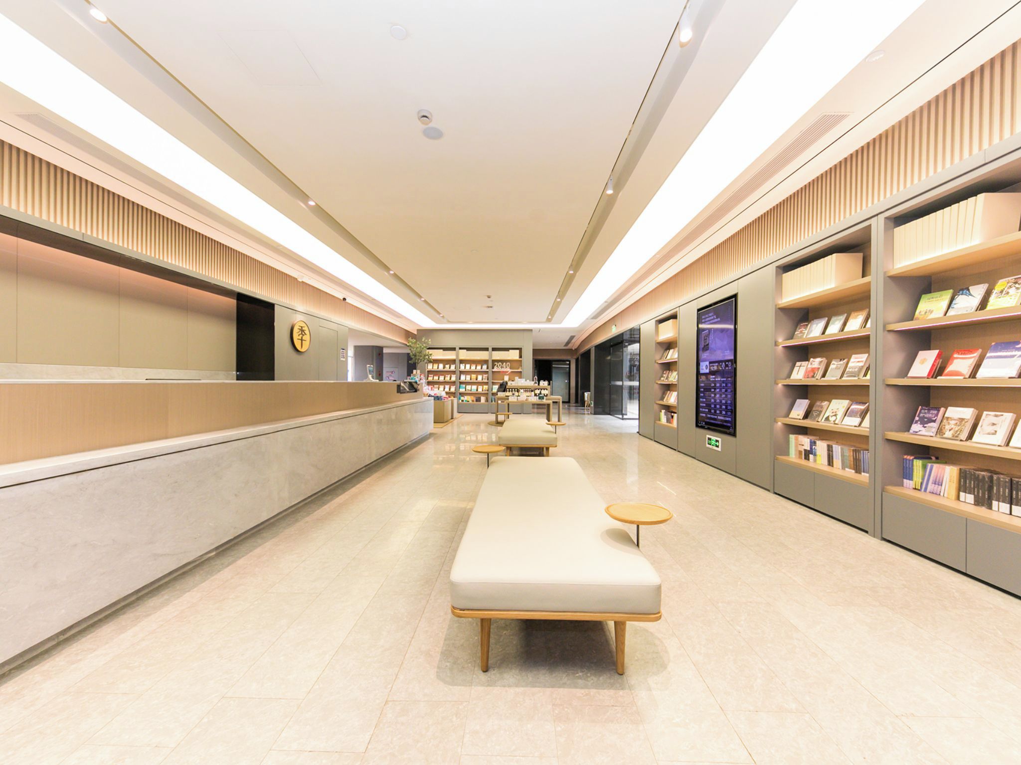 Un moderno y luminoso vestíbulo de hotel con mostrador de recepción, zona de estar y estanterías llenas de libros.