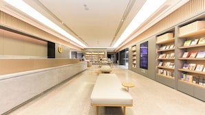 Een moderne, goed verlichte hotellobby met een receptiebalie, een zithoek en boekenplanken.