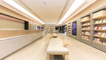 Un moderno y luminoso vestíbulo de hotel con mostrador de recepción, zona de estar y estanterías llenas de libros.