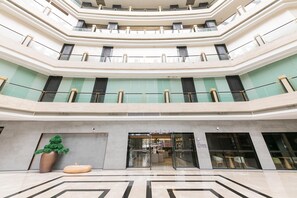 Un hall d’hôtel à plusieurs niveaux, doté d’un atrium central, de rampes en verre et d’un comptoir d’accueil.