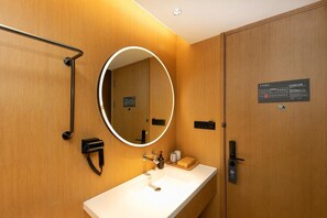 A modern bathroom with a wooden wall, a round mirror, a white sink, a handheld showerhead, and a towel rack. - Ji Hotel (Hefei)