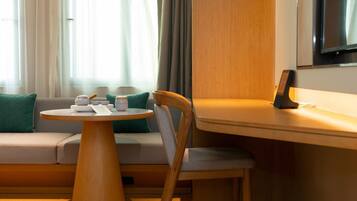 A modern hotel room with a wooden dining table, a comfortable sofa, and a television mounted on the wall.