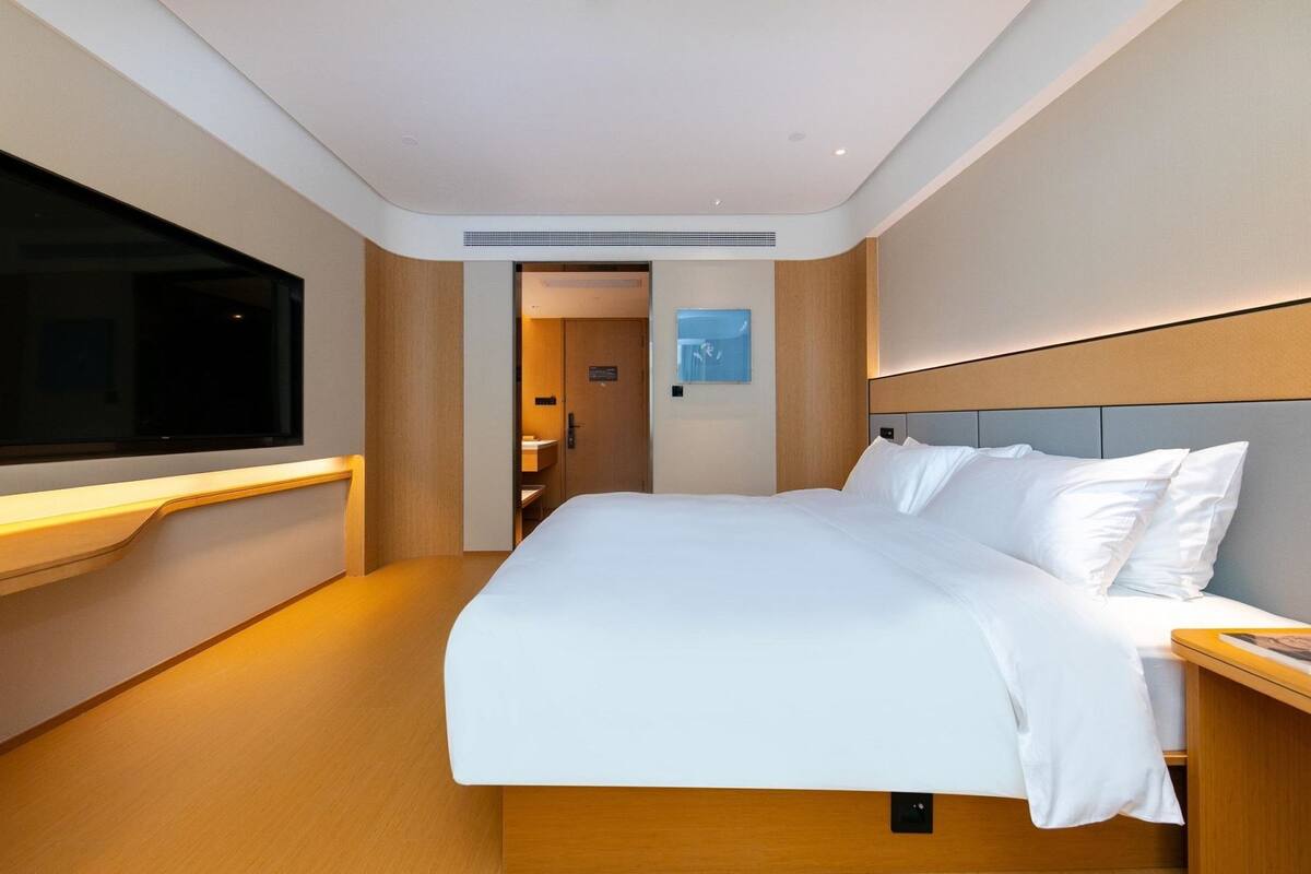 Una camera d'albergo moderna con un grande letto, una TV a muro e una testiera in legno.