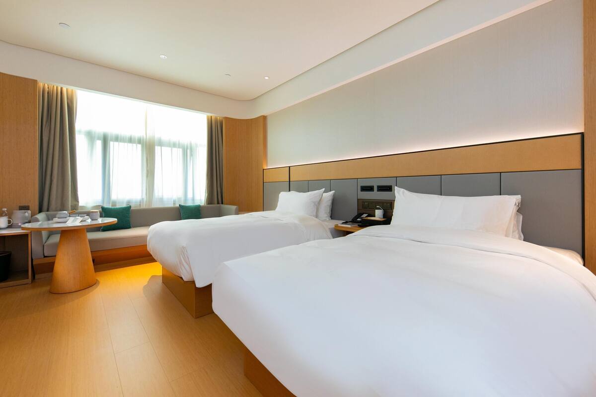 Una camera d'albergo con due letti, un tavolino, un comodino e una finestra con tende.