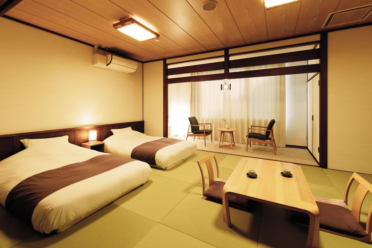 Habitación de hotel con dos camas, una mesa de comedor, sillas y vista a un jardín a través de una puerta corrediza.