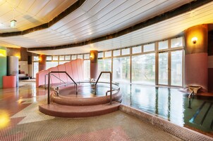 Una amplia piscina interior con una escalera central y vistas al exterior a través de grandes ventanales.