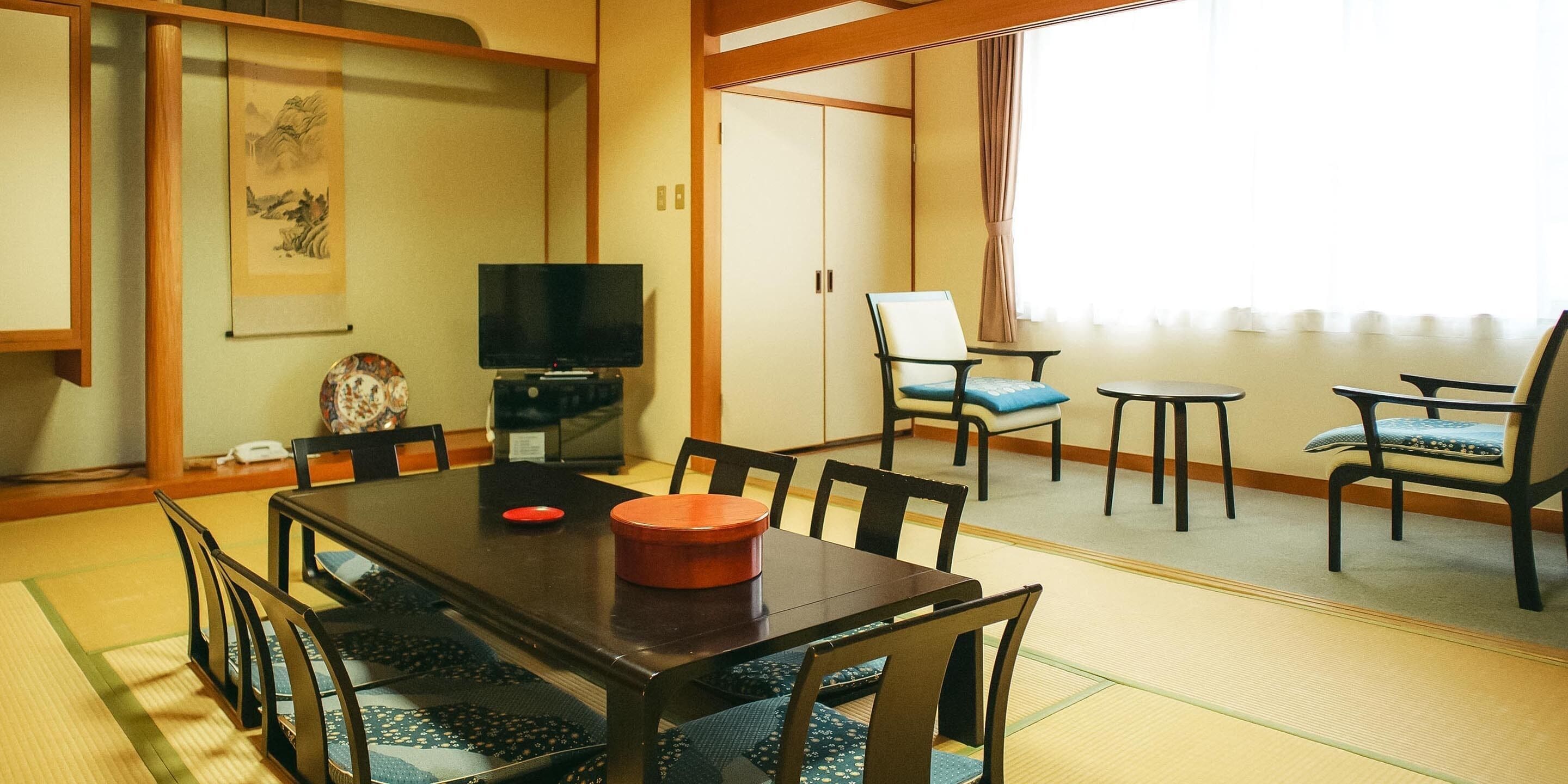 A traditional Japanese-style room with tatami mat flooring, a low table with chairs, a television, and a sliding door.