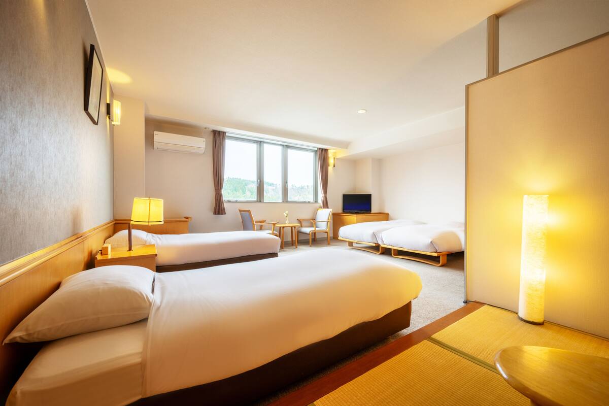 Habitación de hotel con dos camas, televisión, escritorio y ventana con cortinas.