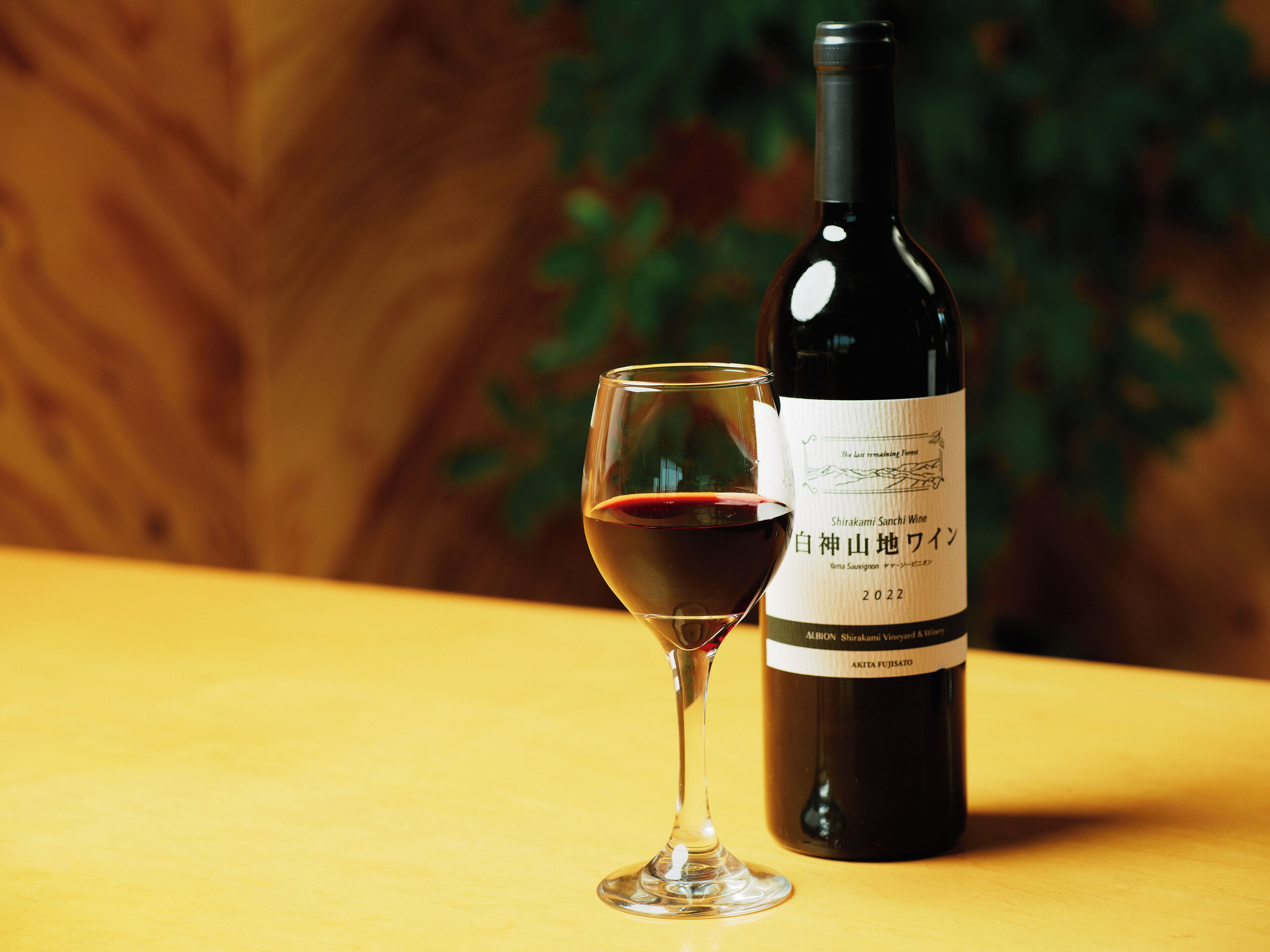 Une bouteille de vin Shirakami Sanchi et un verre de vin rouge sur une table en bois.