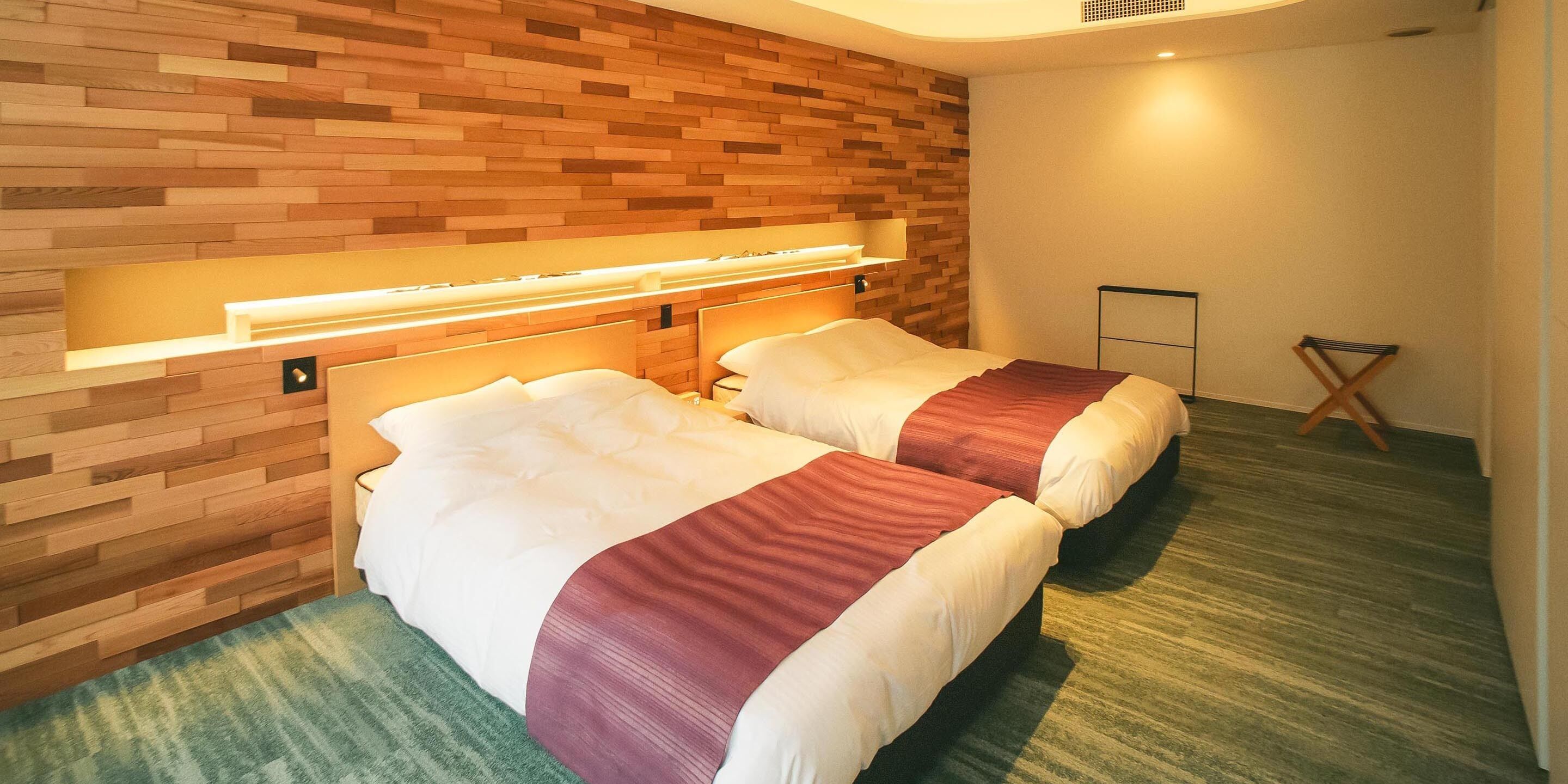 A hotel room with two beds, wooden wall paneling, and a green carpet.