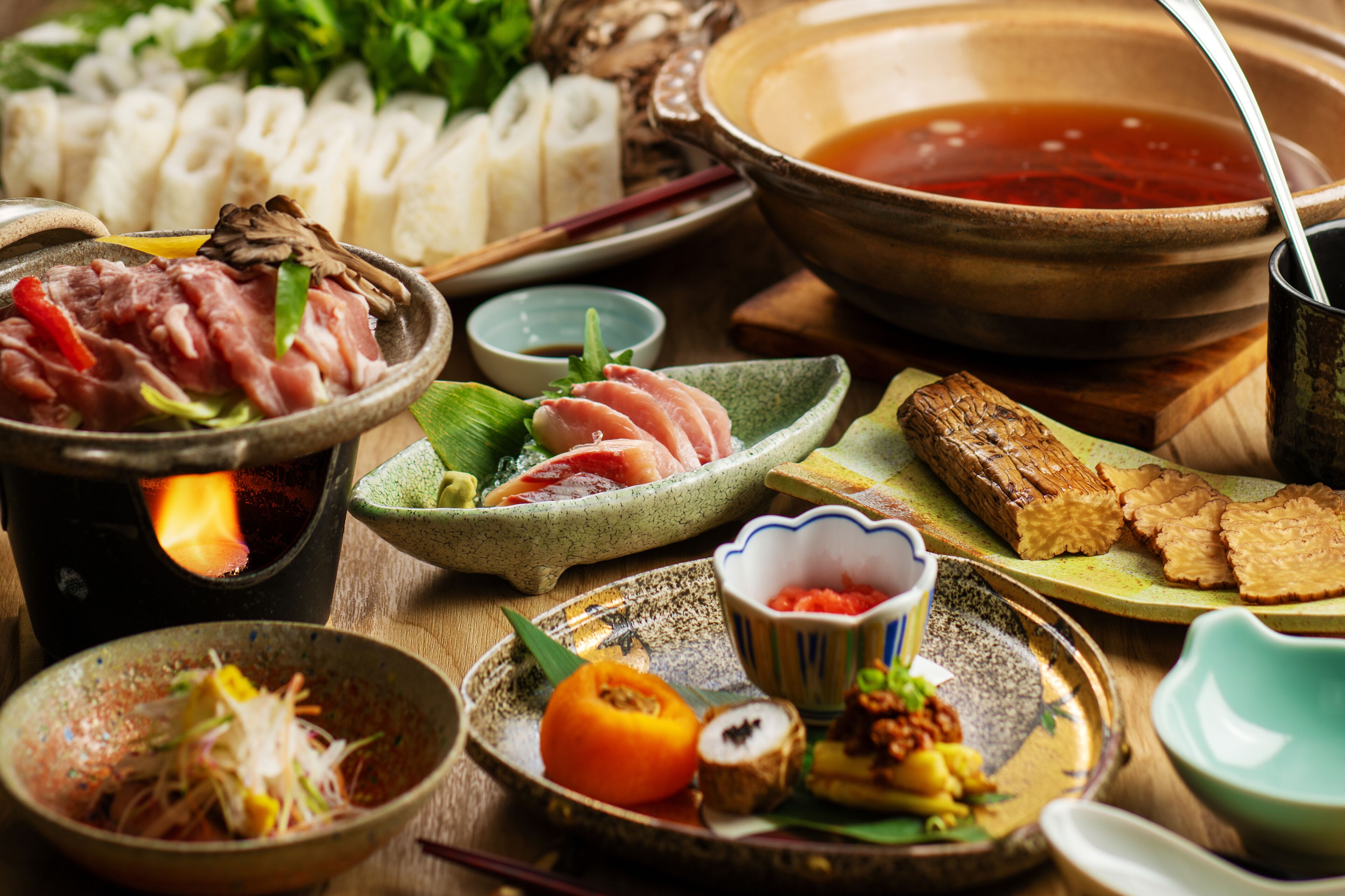 Variedad de platos que incluyen sashimi, verduras y una olla caliente, dispuestas sobre una mesa de madera.