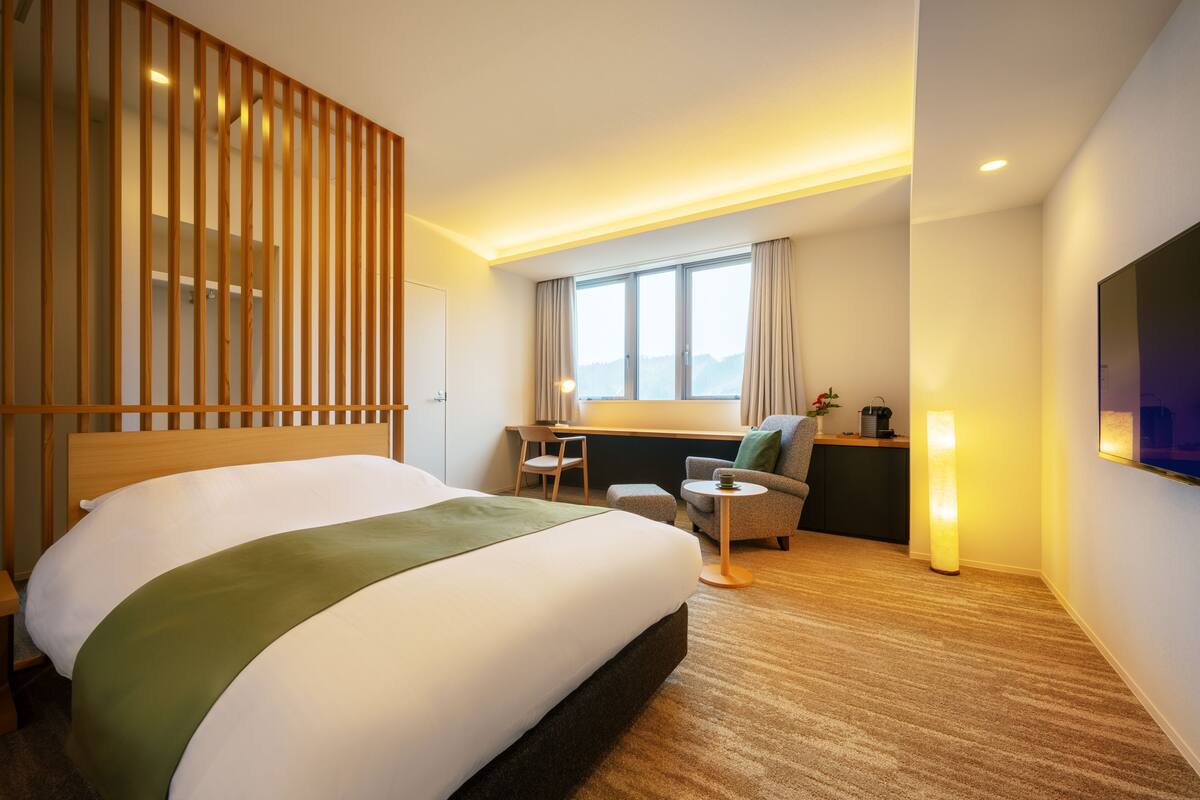 Habitación de hotel con una cama grande, un escritorio, una silla, un televisor y una ventana con cortinas.