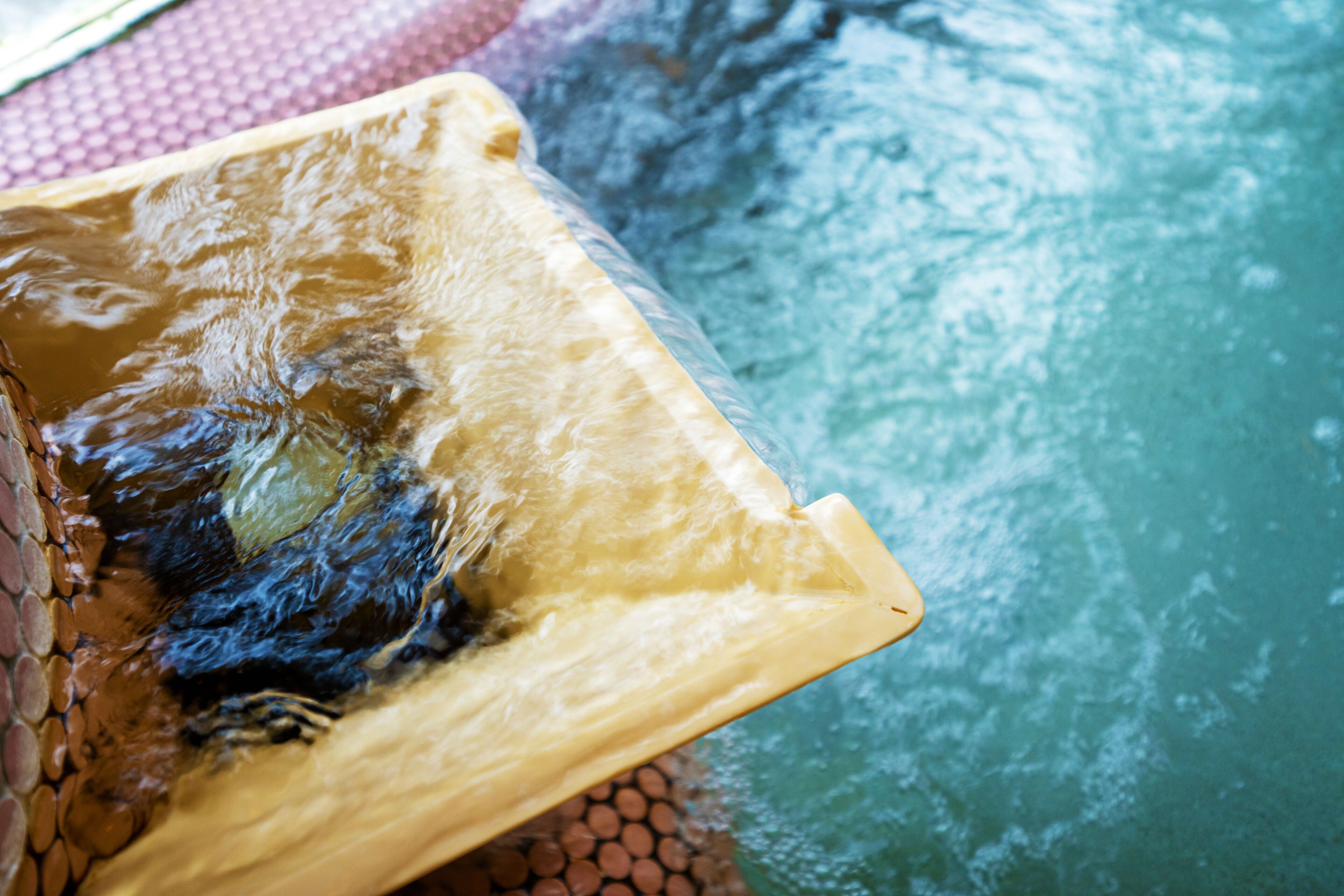 A close-up of a pool edge with water splashing against a tiled surface.