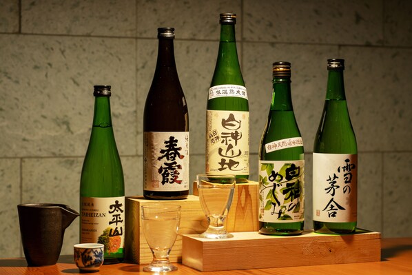 A selection of green bottles with Japanese labels, a small ceramic cup, and a glass on a wooden surface. - hotel yutoria fujisato (Fujisato)