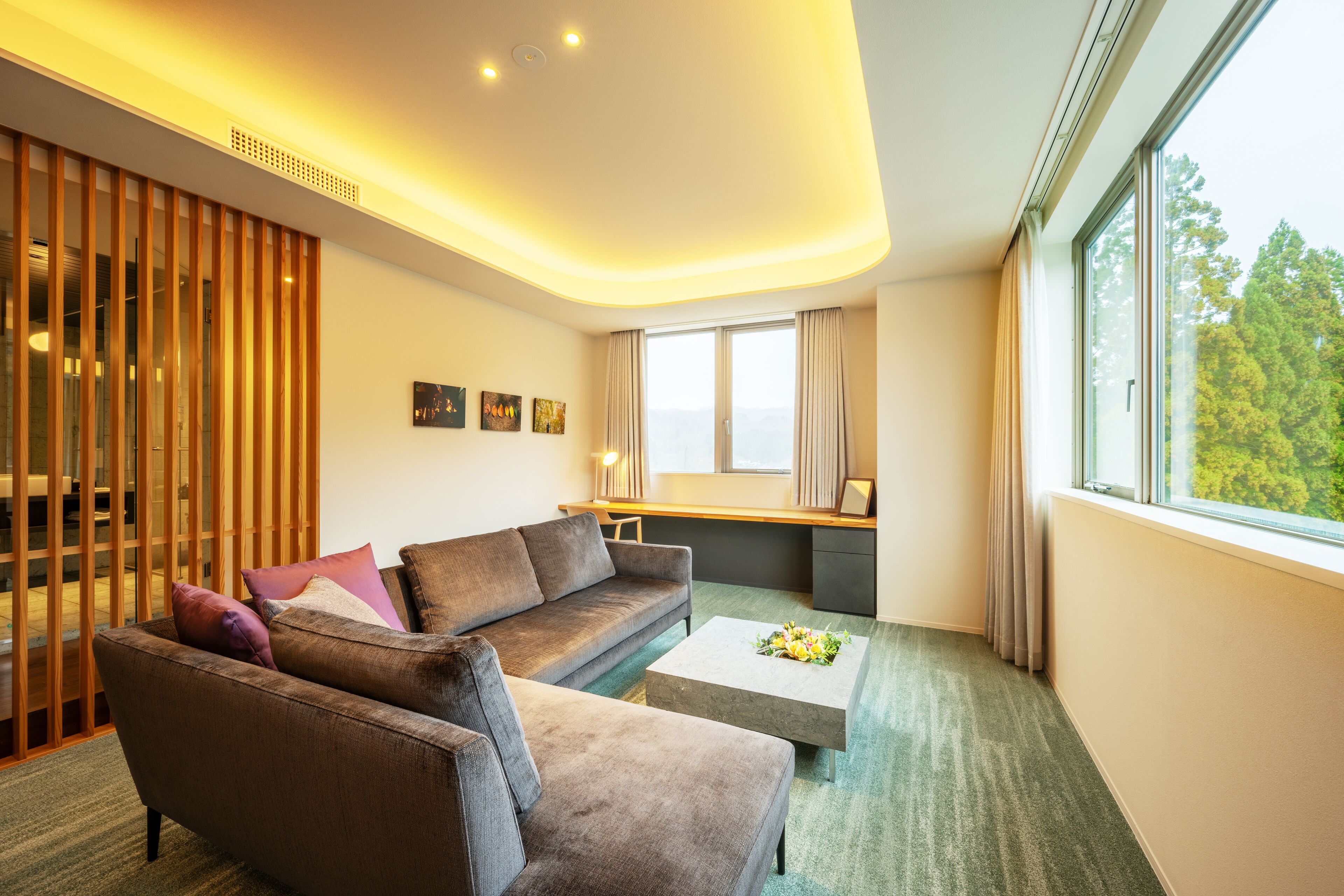Ein modernes Hotelzimmer mit einer Couch, einem Couchtisch und einem großen Fenster mit Blick auf Bäume.