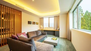 Ein modernes Hotelzimmer mit einer Couch, einem Couchtisch und einem großen Fenster mit Blick auf Bäume.