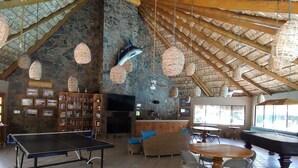 Une pièce spacieuse avec un plafond haut, un mur en pierre, une table de ping-pong, une table de billard et une bibliothèque avec des photos encadrées.