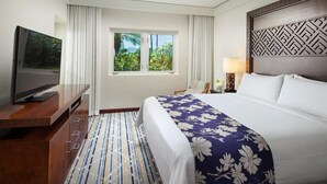 A hotel room with a bed, a TV, a window with curtains, a ceiling fan, and a patterned headboard.