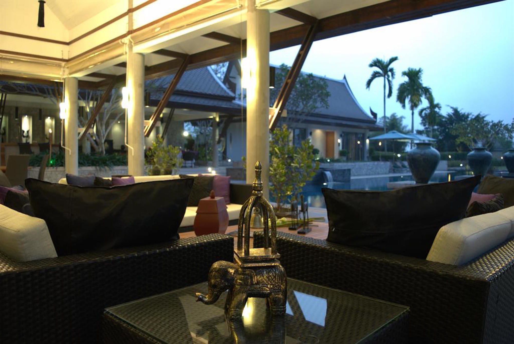An outdoor seating area with wicker furniture and a glass table, overlooking a pool and palm trees.