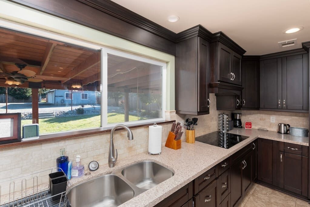 A kitchen with dark cabinets, a double sink, and a window overlooking a backyard.