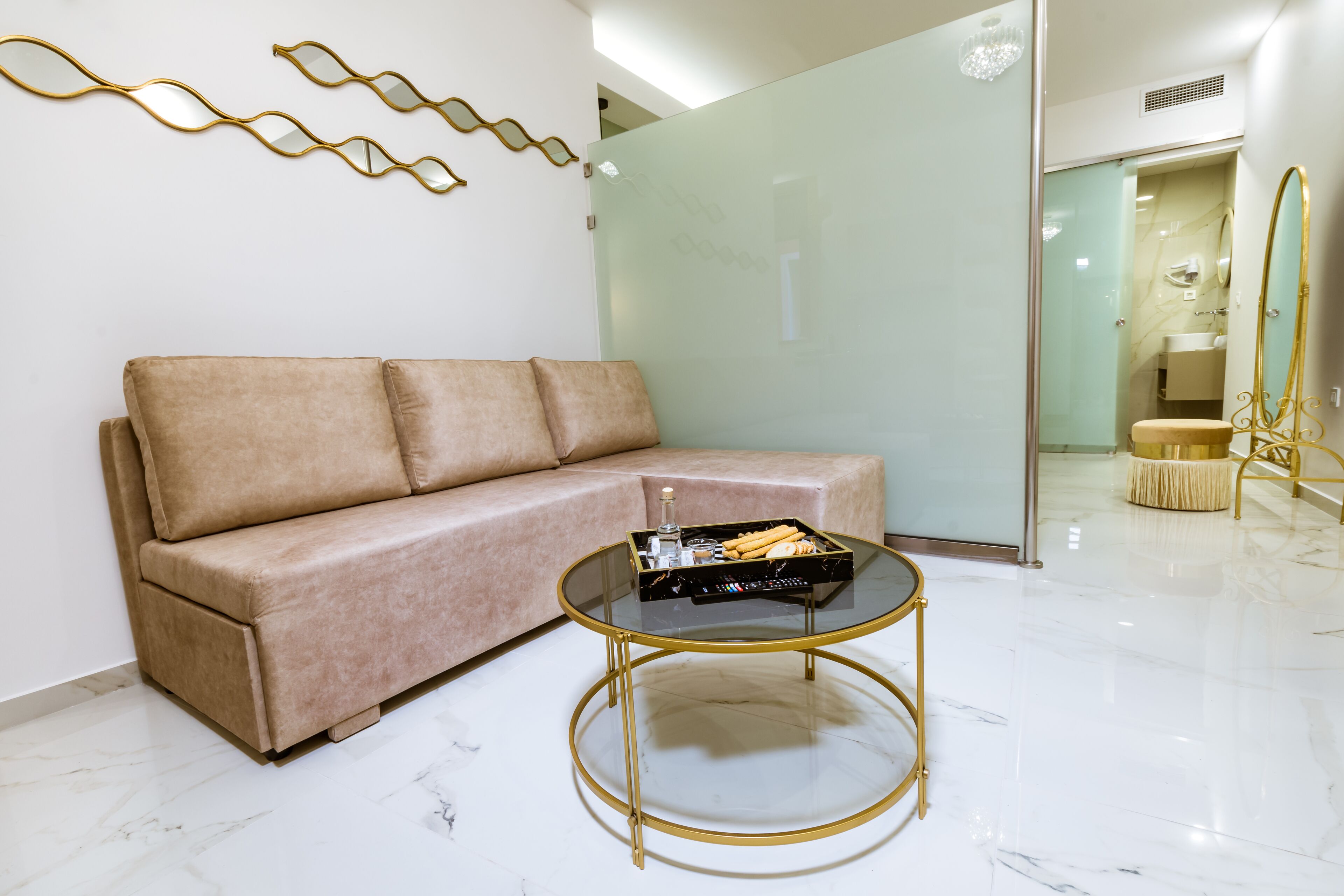 Un interior moderno con un sofá color beige, una mesa de centro de cristal y un espejo con marco dorado.