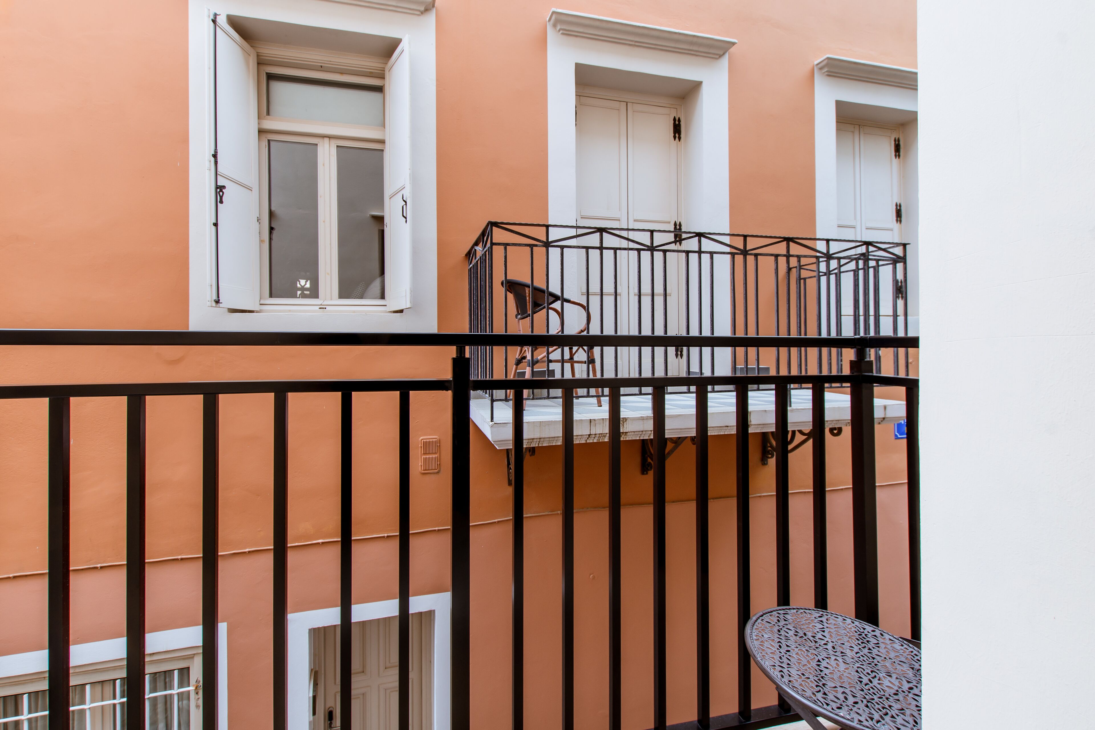 Un balcon avec une rambarde en métal, une chaise et une fenêtre à cadre blanc.
