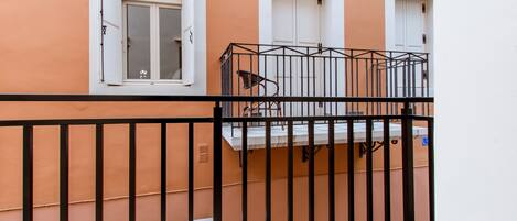 Un balcon avec une rambarde en métal, une chaise et une fenêtre à cadre blanc.