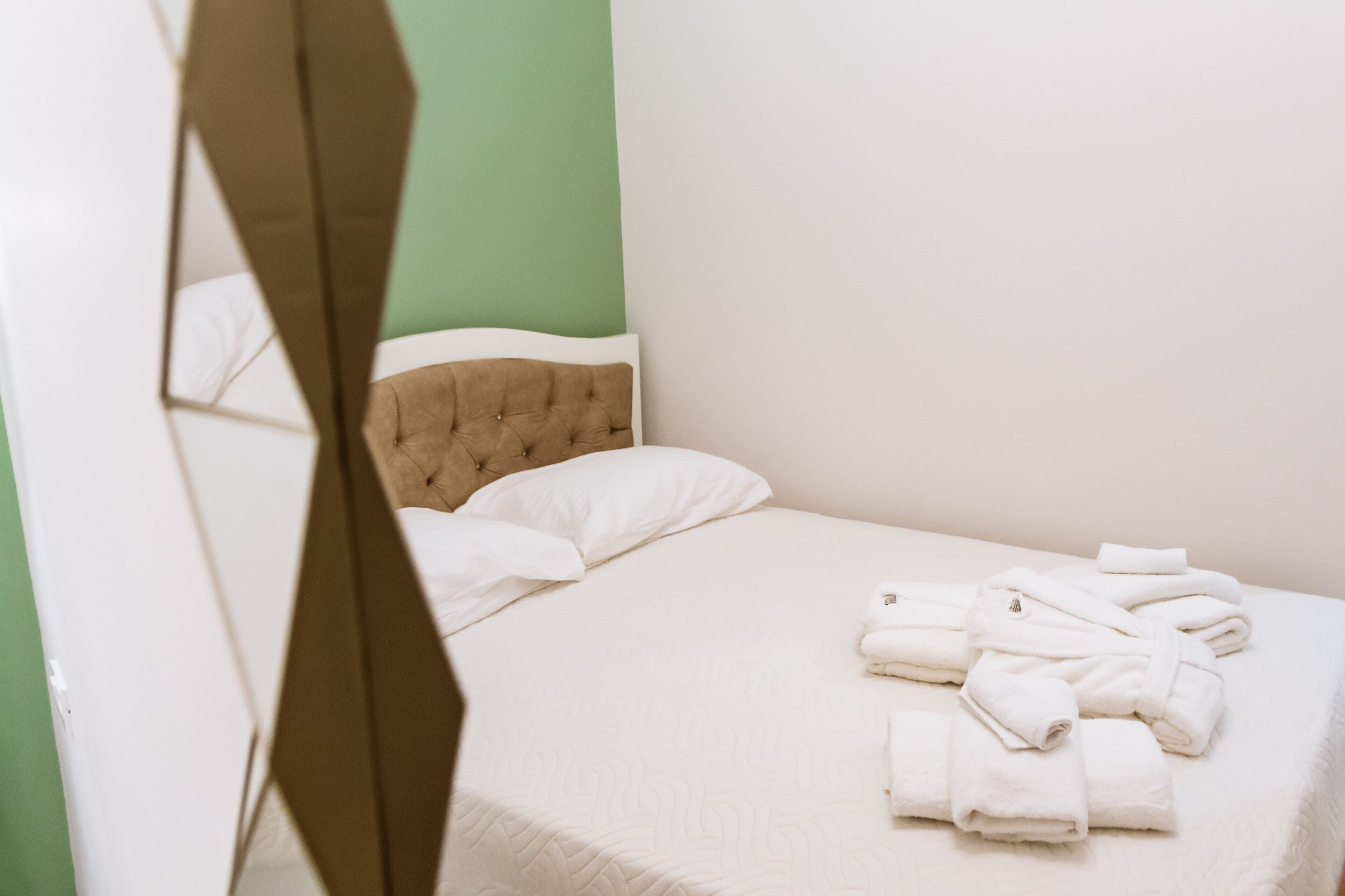 Una cama bien hecha con ropa blanca y un cabecero capitonado, junto con toallas blancas dobladas.