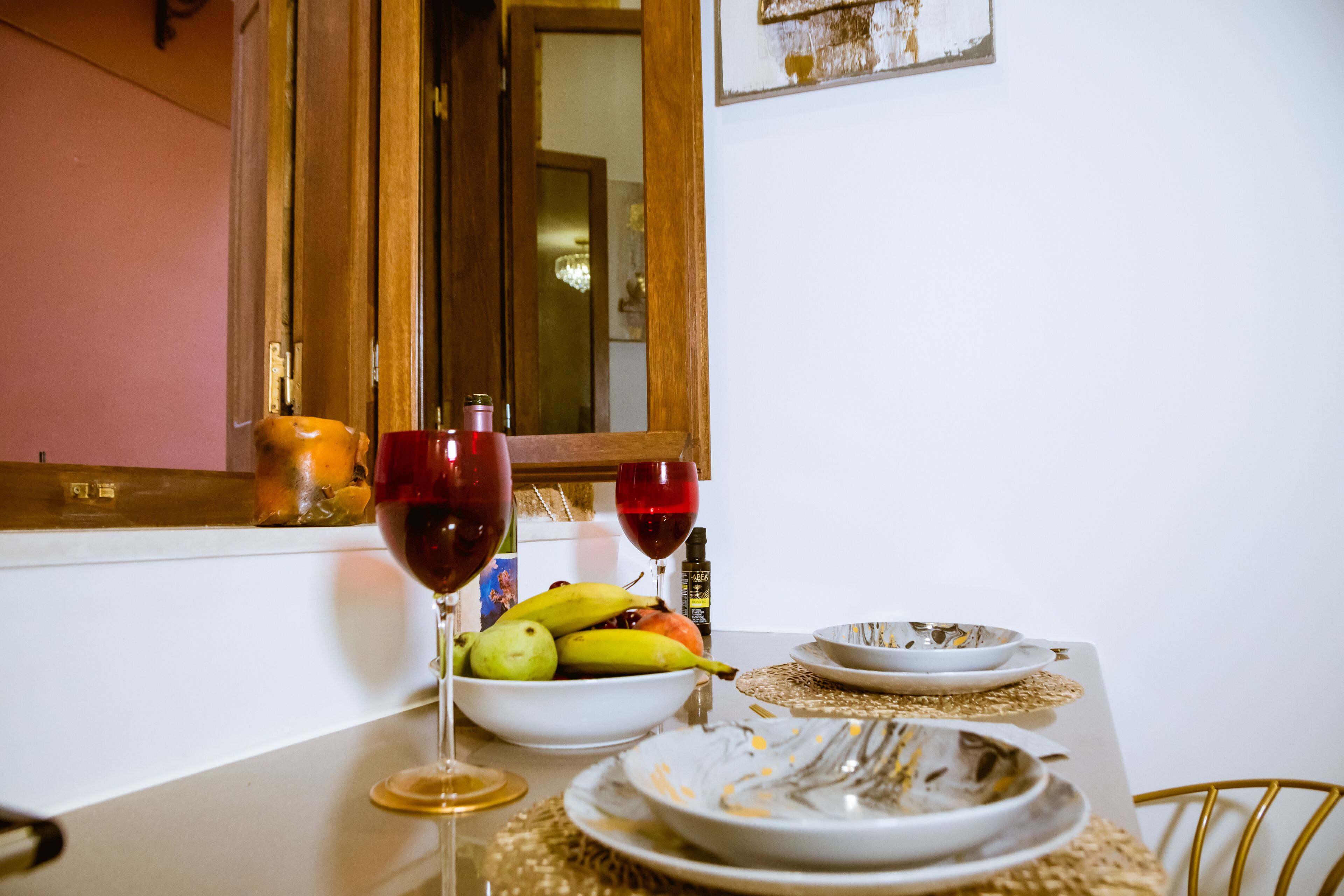 A dining table with a bowl of fruit, two wine glasses, and plates.