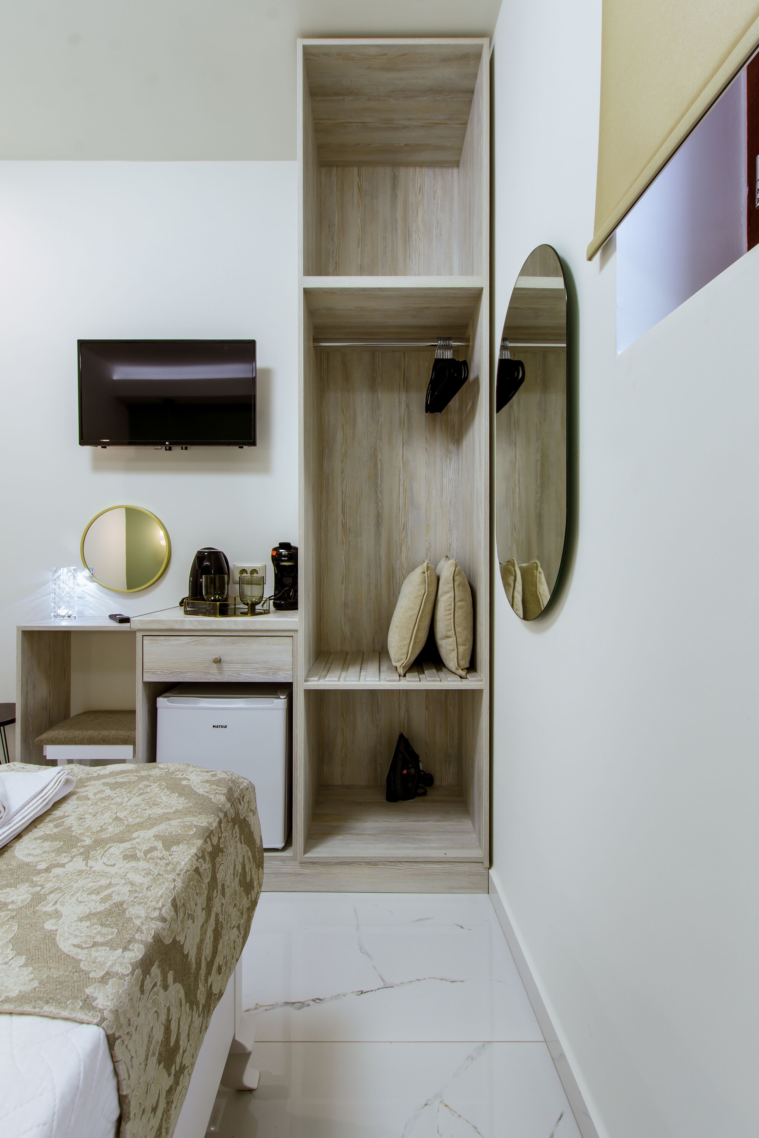 Una habitación de hotel con cama, escritorio con espejo, televisor, armario y refrigerador pequeño.