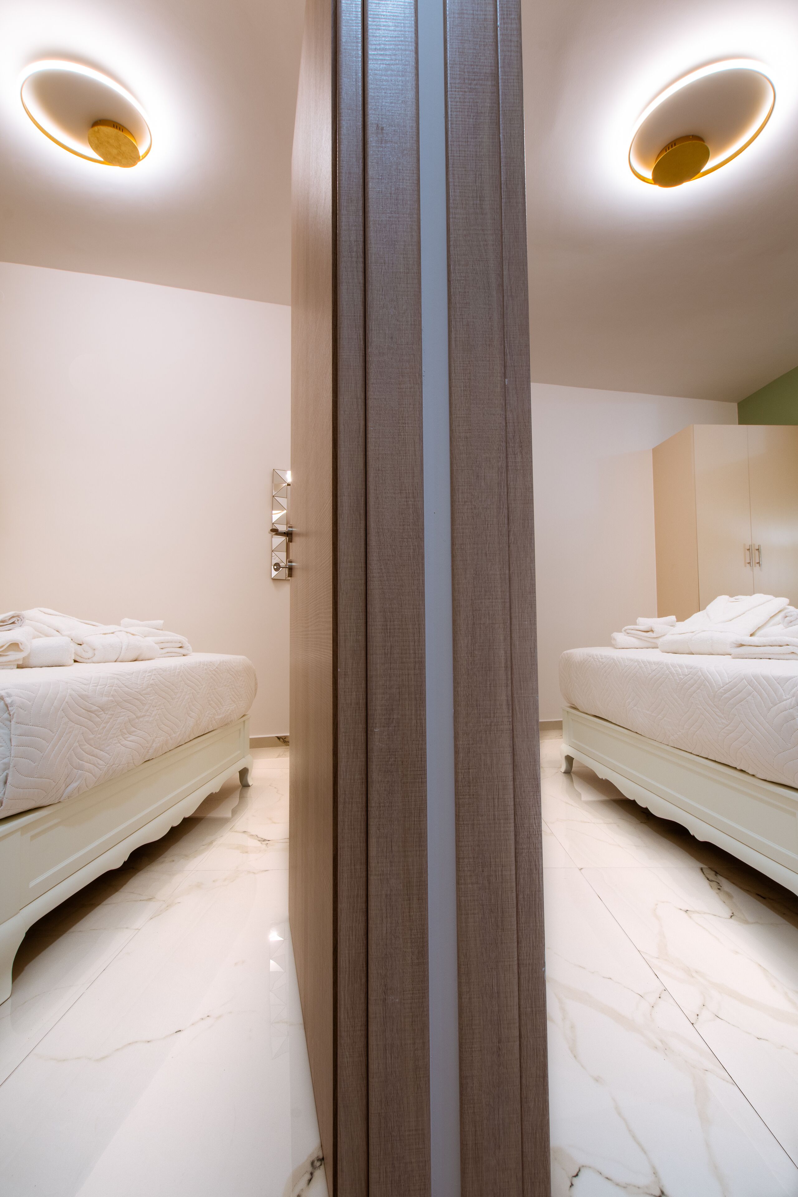 A hotel room with two beds, a wooden wardrobe, and a marble floor.