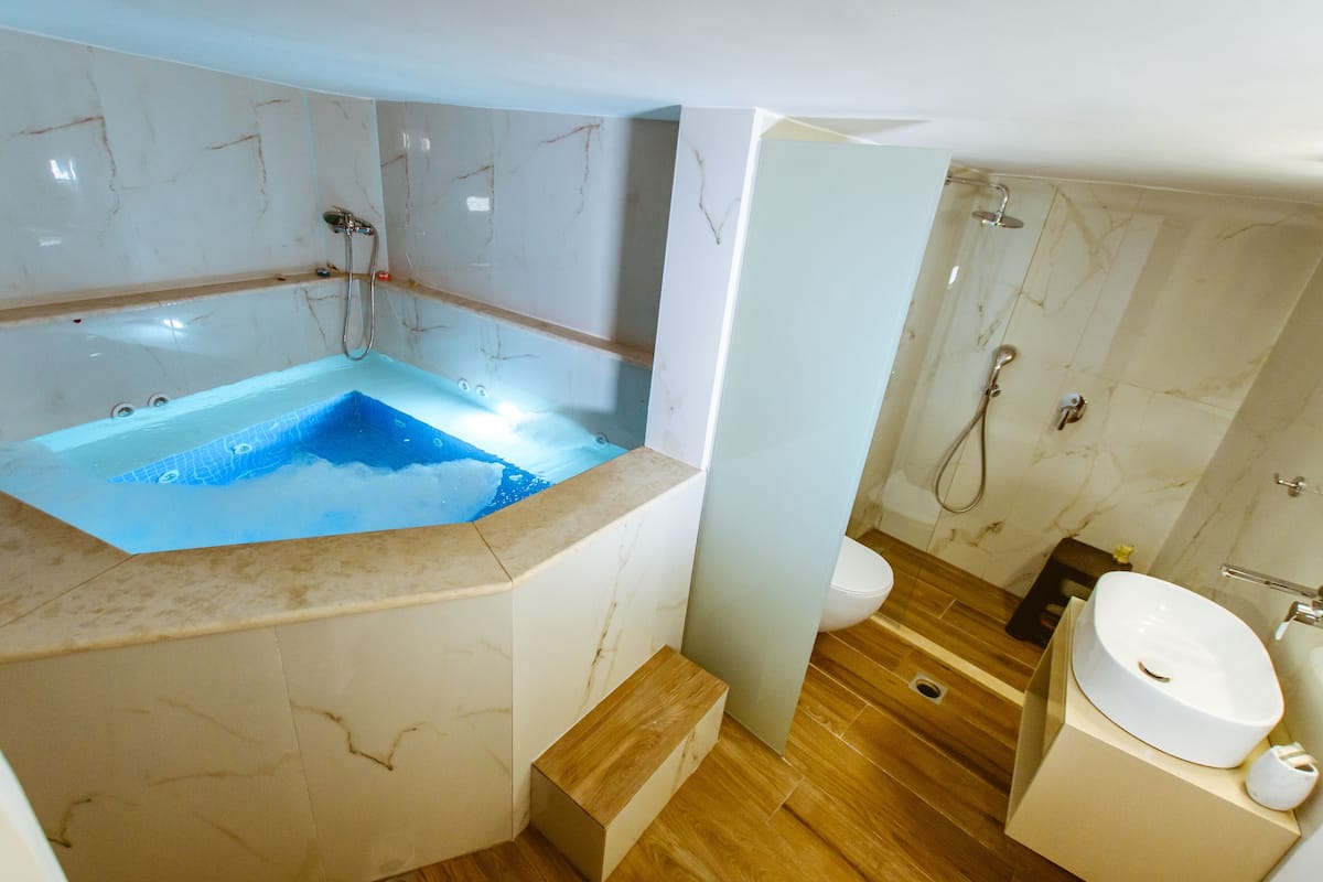 Une salle de bain moderne avec un mur recouvert de carreaux de marbre, une baignoire sur pieds, un meuble-lavabo en bois et une zone de douche séparée.